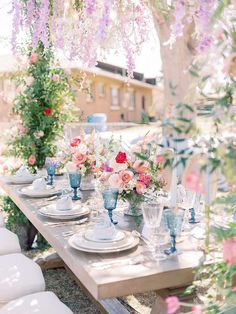 an outdoor table set with plates and vases on it, surrounded by pink flowers