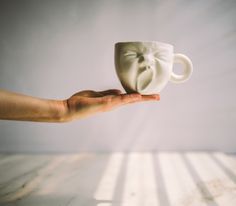 a person's hand holding a white coffee cup with a face on the side