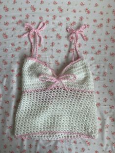 a crocheted bralet with pink bows on the front and bottom, laying on a bed