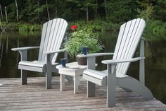 two white adiron chairs sitting on top of a wooden dock