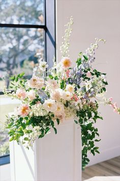 a white vase filled with lots of flowers next to a window