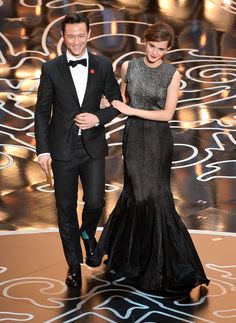 a man and woman in formal wear walking down the stage at an oscars event