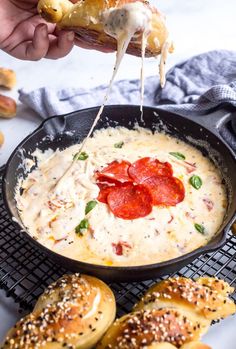 someone is dipping cheese on bread with pepperoni in a skillet and other baked goods