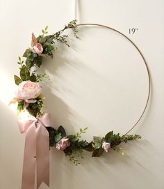 a wreath with pink flowers and greenery is hanging on the wall