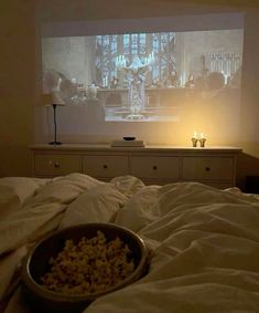 a bowl of popcorn sitting on top of a bed in front of a flat screen tv