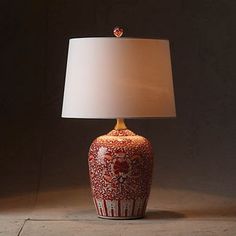 a red and white vase with a lamp on it's side sitting in front of a dark background