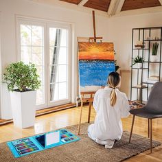 a woman sitting on the floor in front of an easel