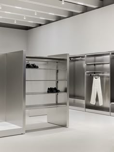 an empty white room with stainless steel closets and clothes hanging on the racks in front of them