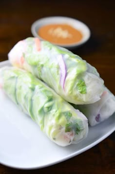 two spring rolls on a white plate with dipping sauces in the bowl behind them