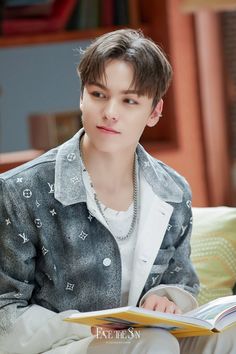 the young man is reading a book while sitting on a couch with his hands in his pockets