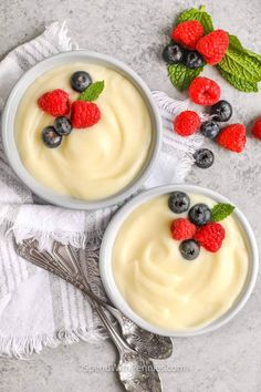 two bowls filled with yogurt and berries on top of a white table cloth