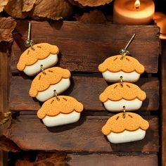 four cookies shaped like mushrooms hanging from hooks on a wooden board with candles in the background