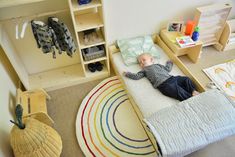 a small child laying on top of a bed in a room with toys and bookshelves