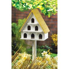 a white bird house sitting on top of a wooden pole in front of some yellow flowers