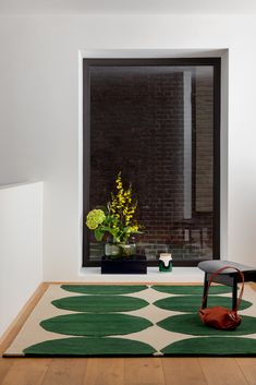 a room with a rug, chair and vase on the floor in front of a window