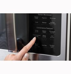 a finger is pointing at the controls on a stainless steel microwave with its door open