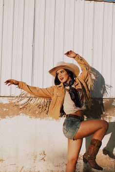 a woman in cowboy boots and a hat posing for the camera with her arms outstretched