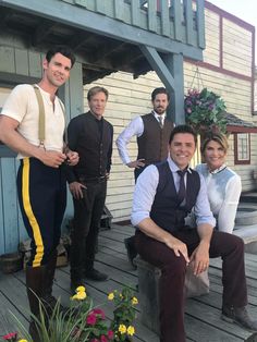 a group of men standing and sitting on top of a wooden deck next to each other