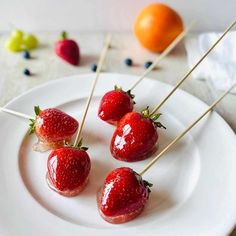 four strawberries are on a white plate with toothpicks