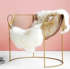 a chair that has some fur on it and is sitting in front of a pink wall