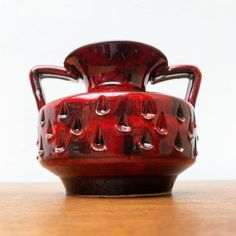 a red vase sitting on top of a wooden table with drops of water in it