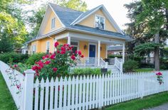 a yellow house with white picket fence and red roses