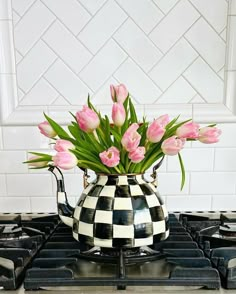 pink tulips are in a black and white checkered pitcher on the stove