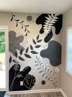 a wall painted with black and white flowers, leaves and plants on the side of it