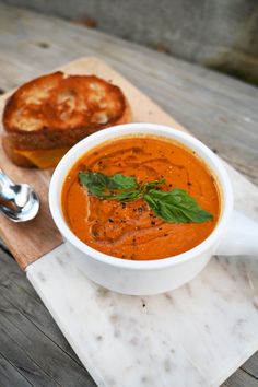 a bowl of tomato soup with bread on a cutting board next to it and a spoon