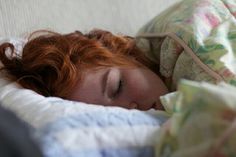 a red headed woman is sleeping under a blanket on a bed with her eyes closed