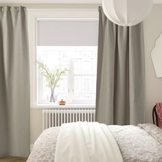 a bedroom with a white bed and gray curtains in front of a window that has a plant on it