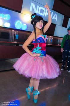 a woman in a pink and blue dress posing for the camera with her hand up