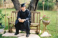 a man sitting on top of a wooden bench wearing a graduation gown and holding a tassel