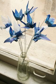 blue origami flowers in a glass vase on a window sill