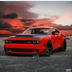 a red and black car parked on top of a parking lot next to the ocean