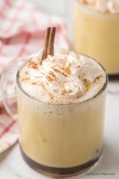 two mugs filled with whipped cream and cinnamon on a white tablecloth next to each other