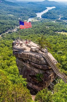 an american flag flying on top of a rock formation in the middle of a forest