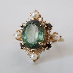 an oval green gemstone surrounded by pearls and other jewelries sits on a white surface