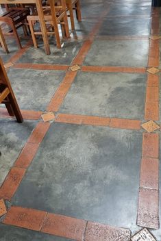 the floor is made out of cement and has orange tiles on it, along with wooden chairs