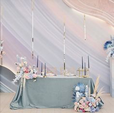 a table with flowers and candles on it in front of a wall decorated with white, blue and pink flowers