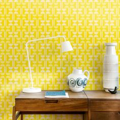 a table with a lamp and vase on it next to a wallpapered background