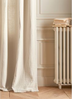 a white curtain is hanging in front of a radiator and wooden flooring