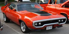 an orange muscle car parked in a parking lot next to other classic cars and people