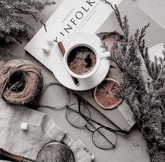 a cup of coffee sitting on top of a table next to some oranges and yarn