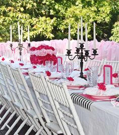 a long table is set with white chairs and pink flowers on the centerpieces