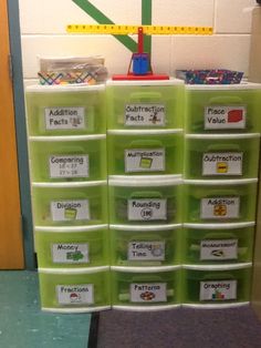 a classroom desk with lots of green bins on top of it and a ruler hanging from the wall