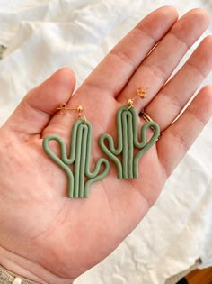 a person is holding some type of cactus earrings in their left hand, with the word cactus written on it