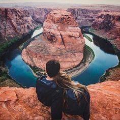 a man sitting on top of a cliff next to a river