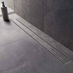 a bathroom with grey walls and flooring next to a soap dispenser