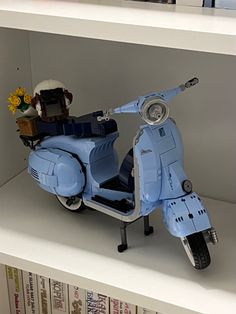 a toy scooter is on display in a bookcase with flowers and books